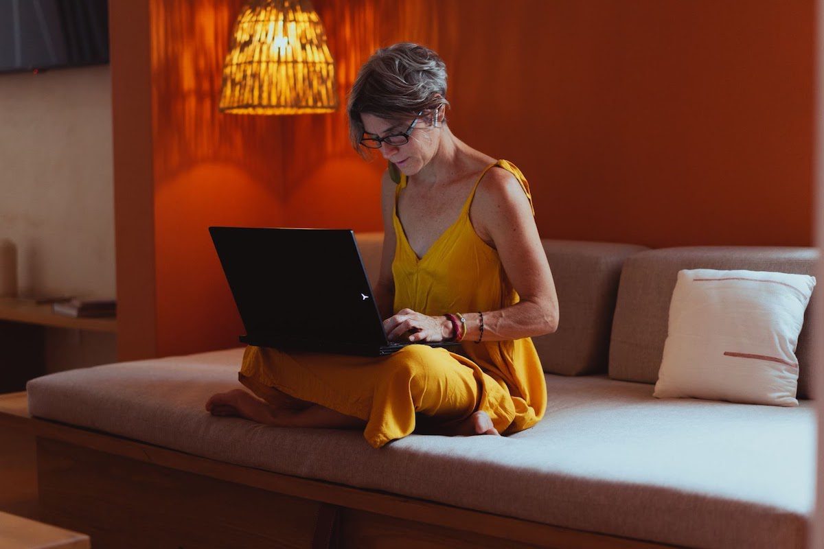 A 50-year-old woman wearing a yellow dress sitting on her bed using a laptop  How to Go Back to College at 50