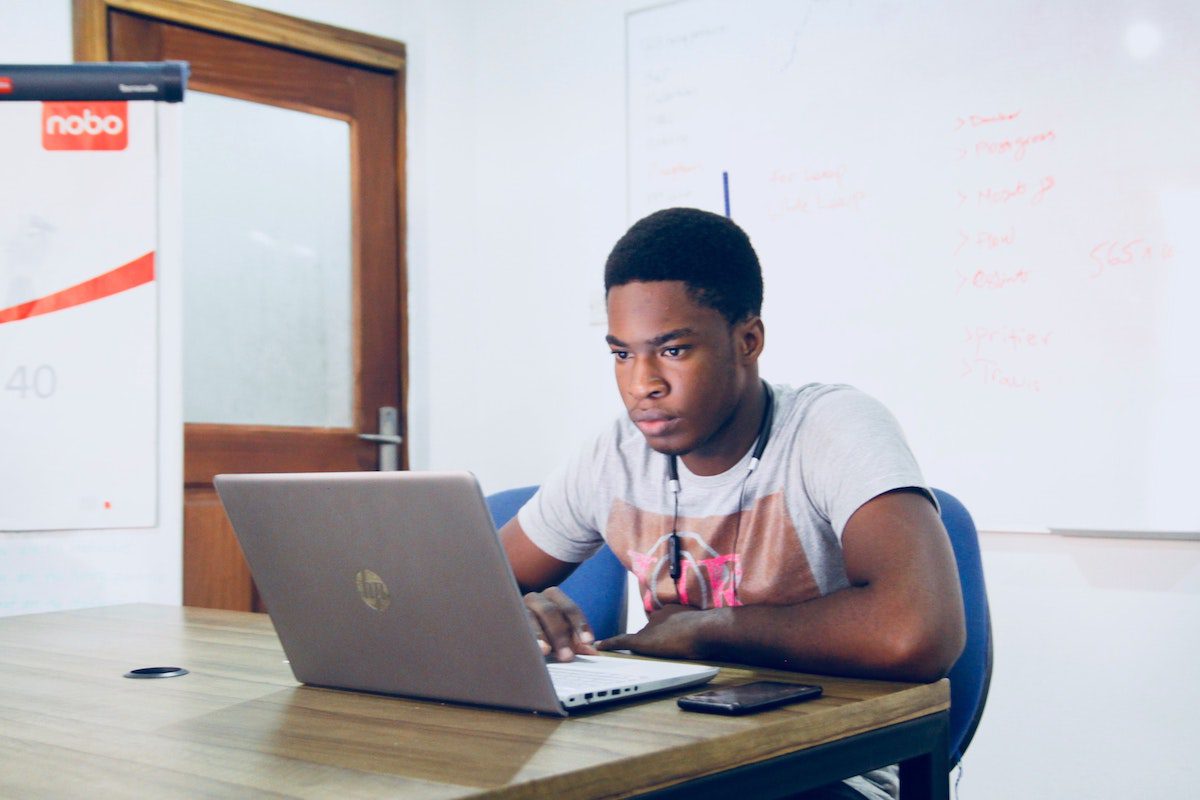 Man in a gray shirt sitting at a desk with a laptop, studying in a coding bootcamp with housing options.