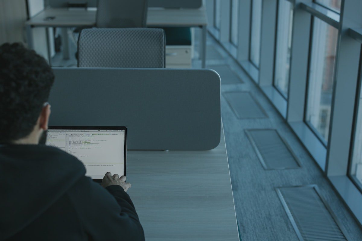 A student in a library sits at a desk with his laptop typing Python code.