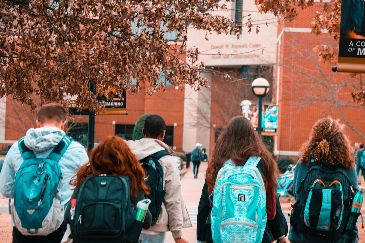 A rear view of four students with backpacks walking toward a computer science university building