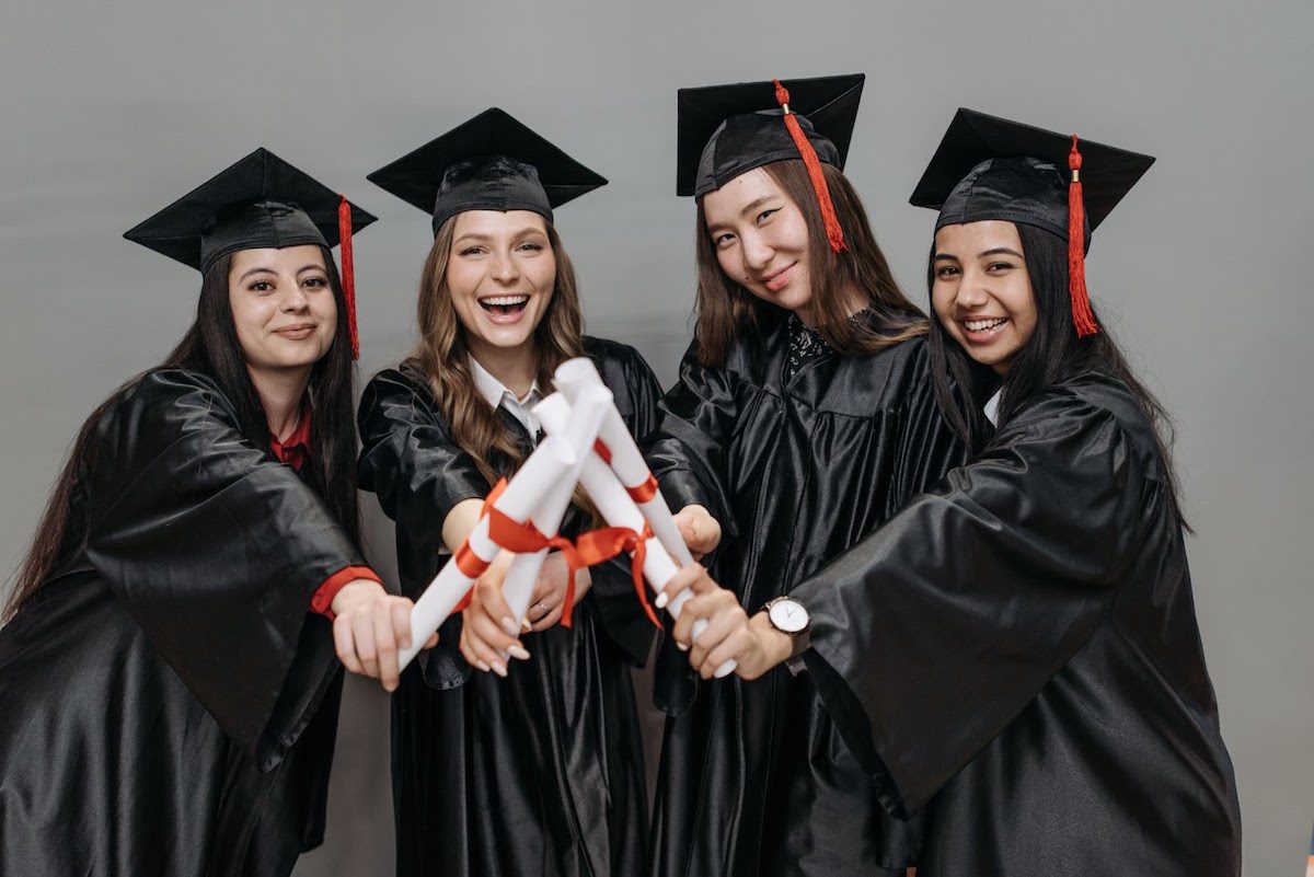 A group of women in their graduation gowns holding their symbolic degrees rolled up and tied with a ribbon Best Online Management Information Systems Bachelor's Degrees 