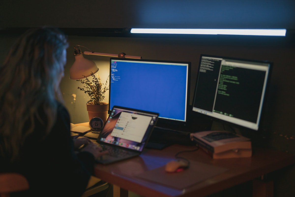 A graduate student programming code on three computer screens