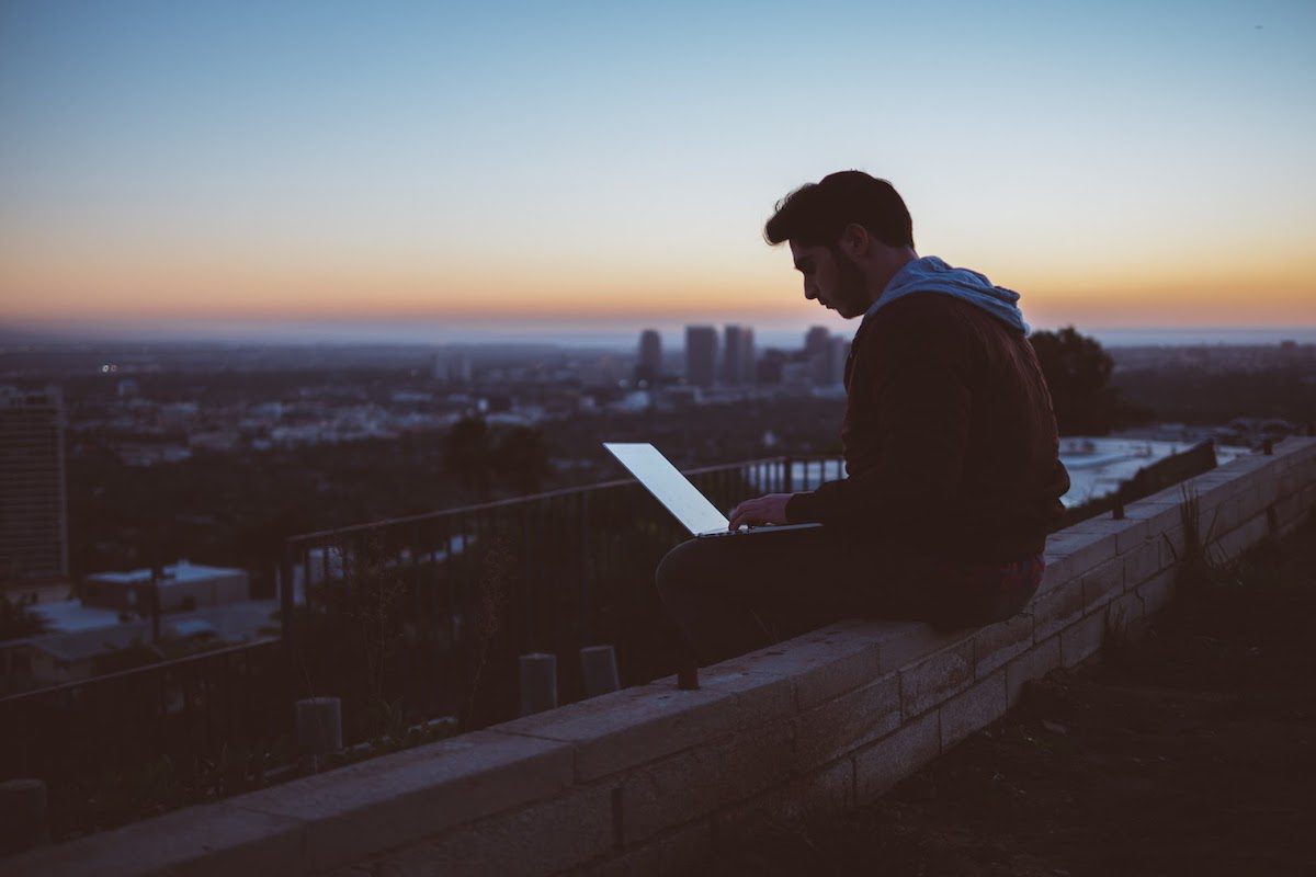Man studying on his laptop with a view of a city skyline at dusk. 