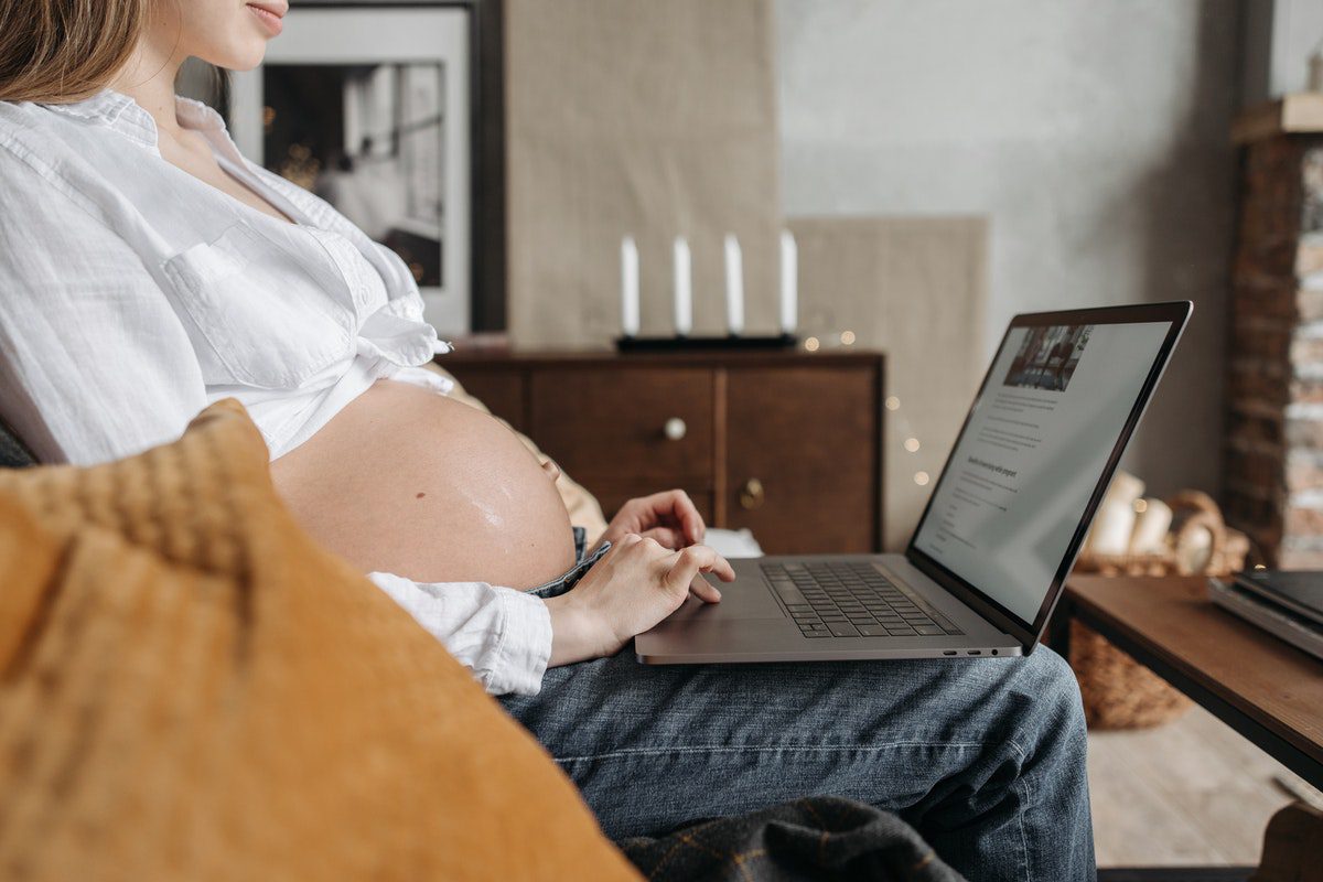 A pregnant woman reading on her laptop.
