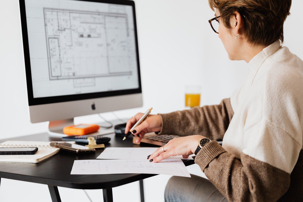 A woman with a pen and paper, looking at a floor plan on a computer