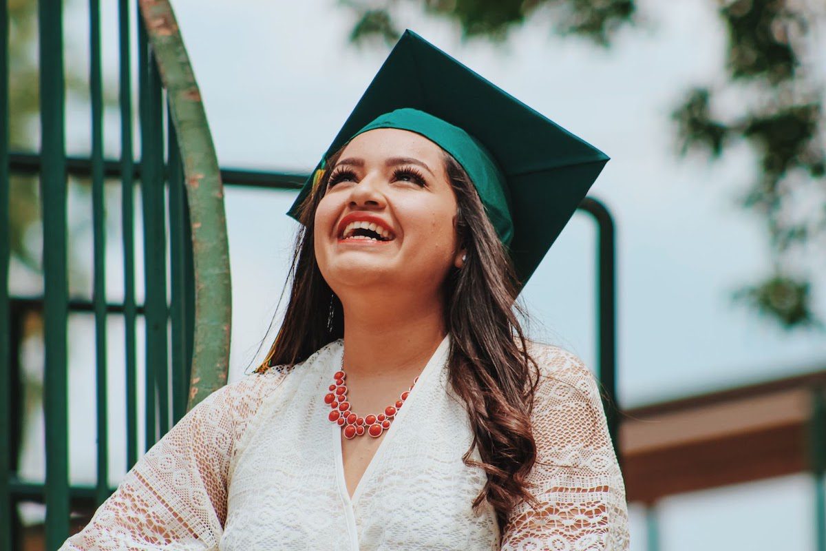 A very happy woman wearing a green graduation cap and white dress