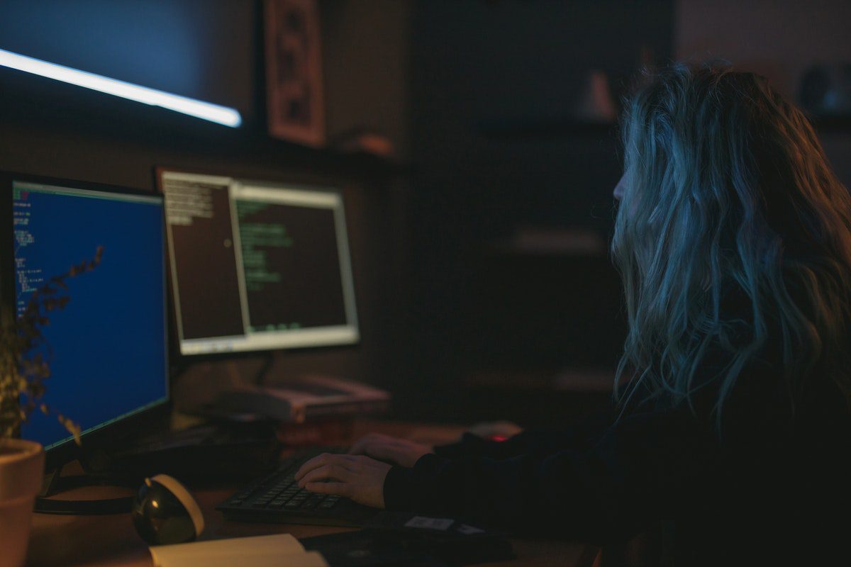 A female ethical hacker working in front of two computer screens