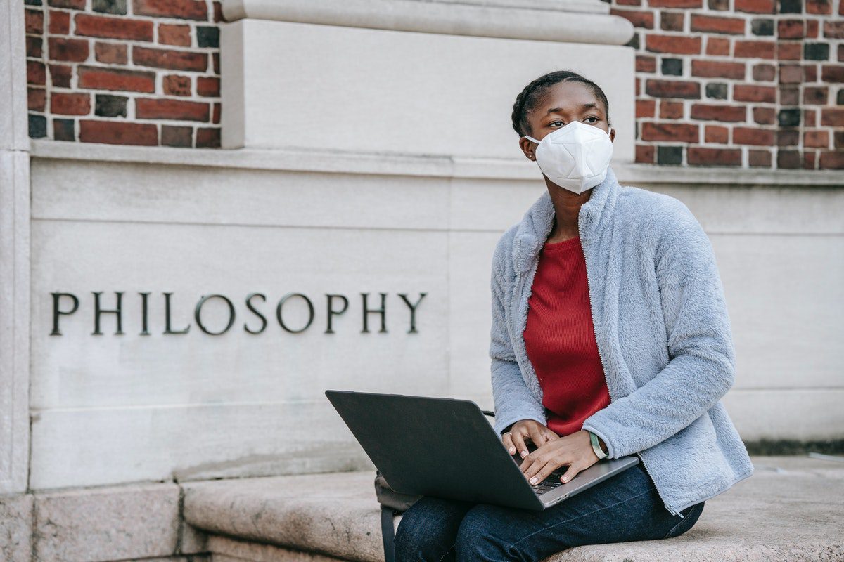 A female student studies on a laptop computer outside a university campus philosophy department building