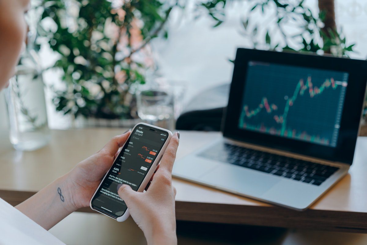 A financial analyst comparing charts on a phone and laptop.