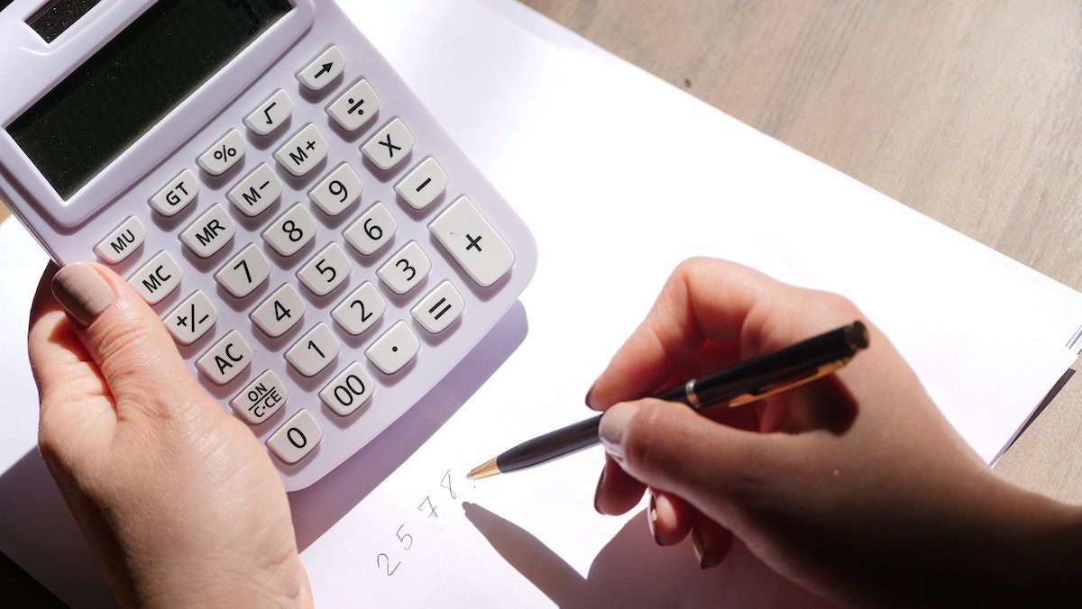 A person doing math holding a calculator and a pen 