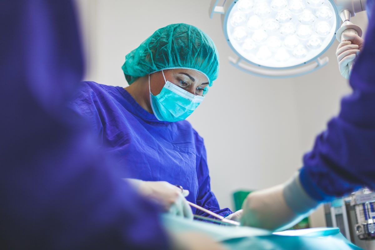 Person wearing a surgical mask, surgical cap, and scrubs in an operating theater.