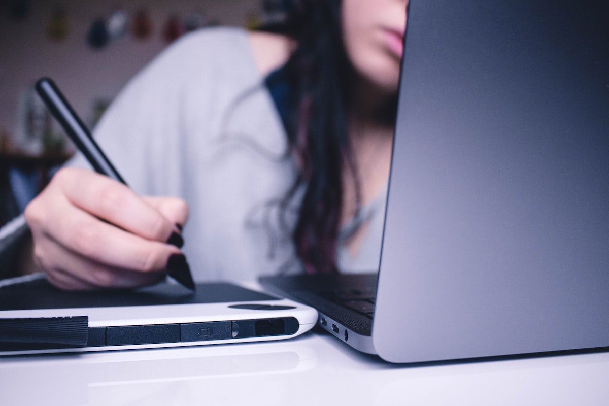 A student taking notes on a tablet while working on a laptop.