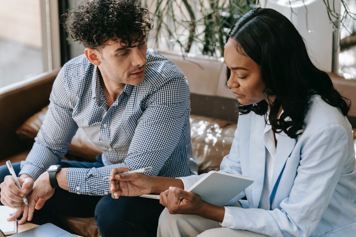 Two people holding a notepad and a pen in a discussion