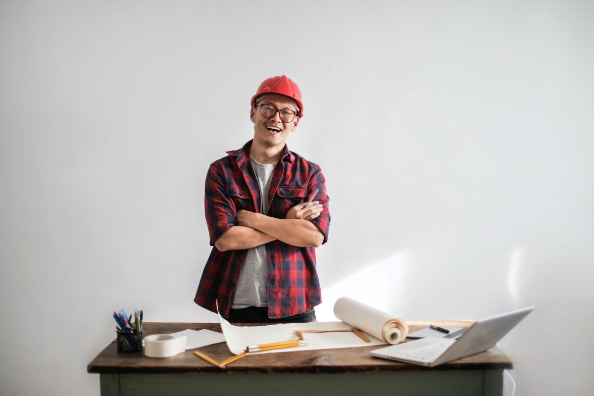 A man in a hard hat laughing while looking at design specifications and a laptop.