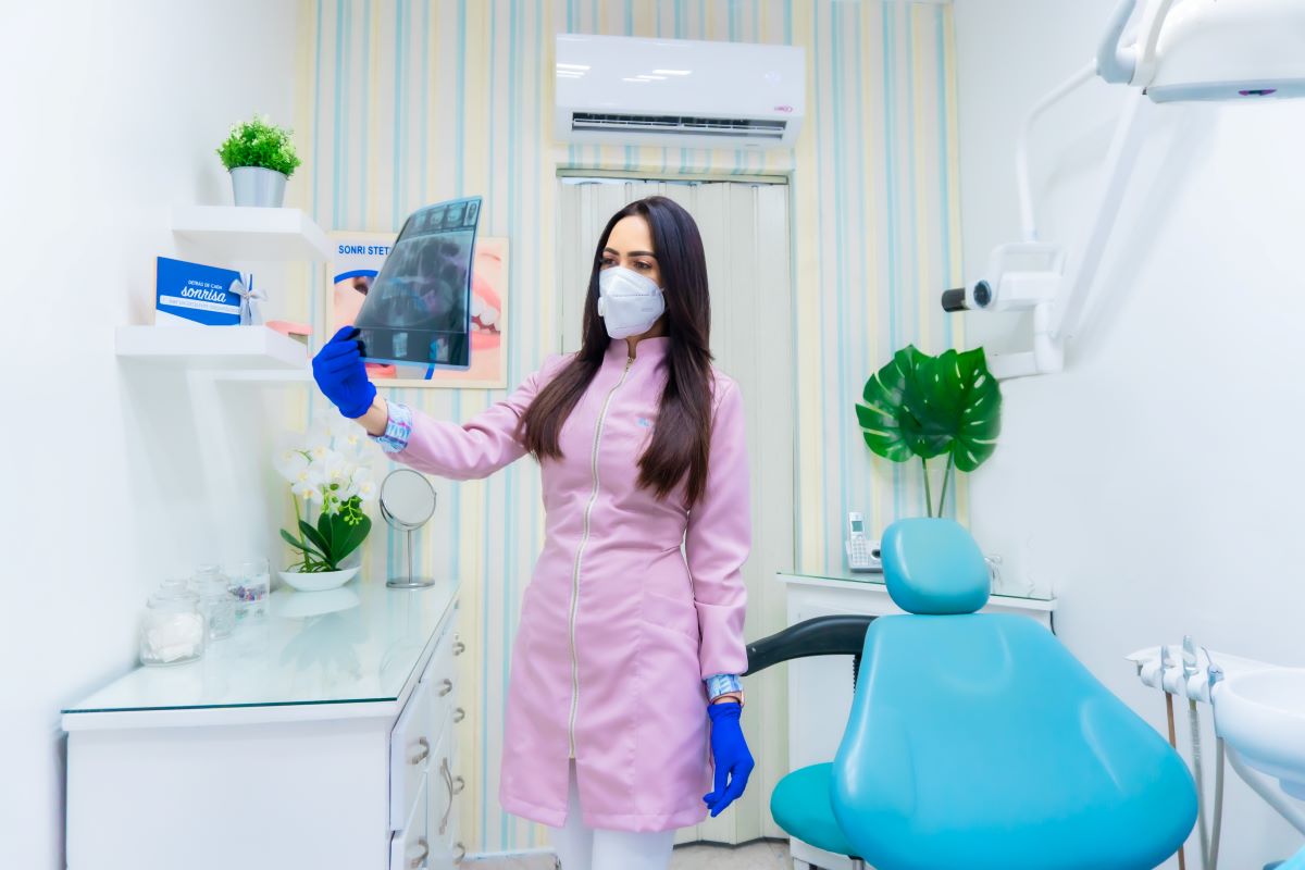 An orthodontist in an office with dental equipment inspecting an X-ray of a jaw