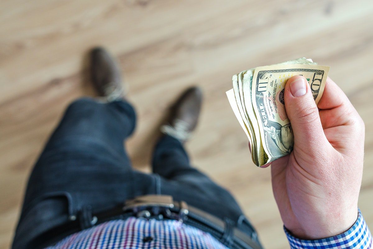 A person holding several folded $10 banknotes