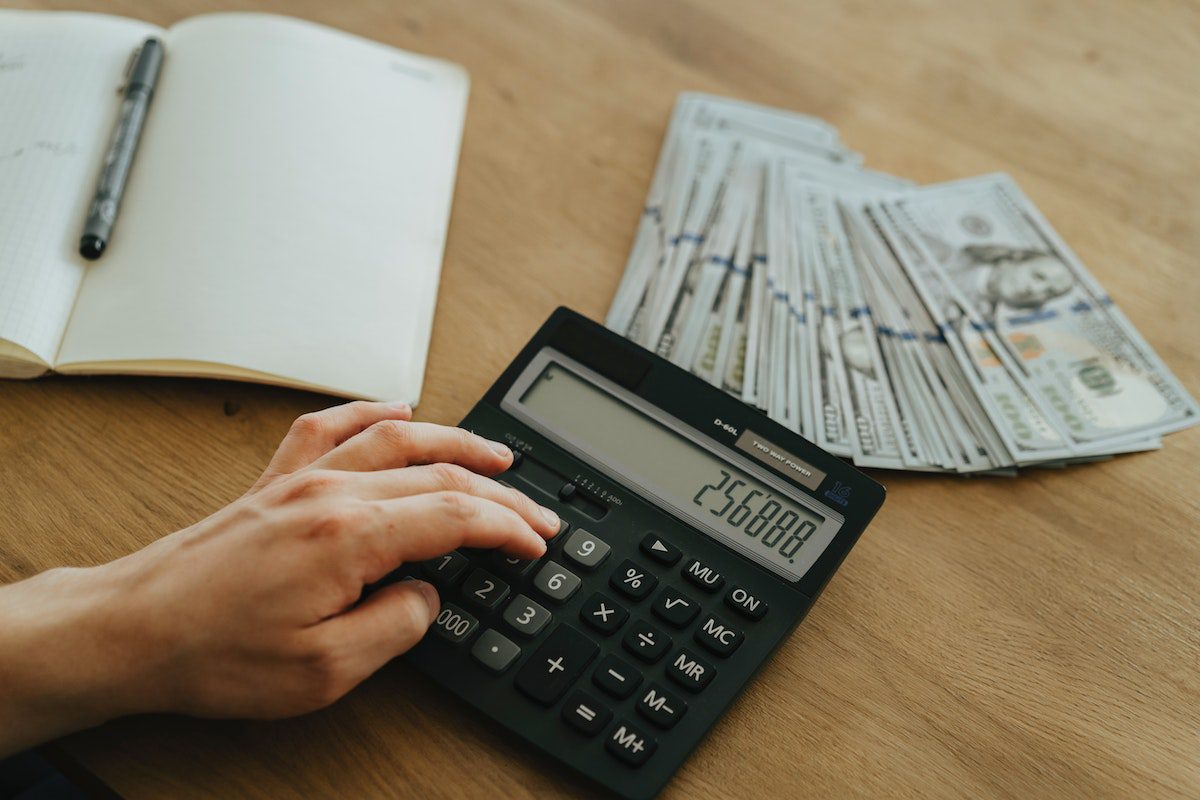 Someone using a calculator with a notebook, pen, and cash on the desk