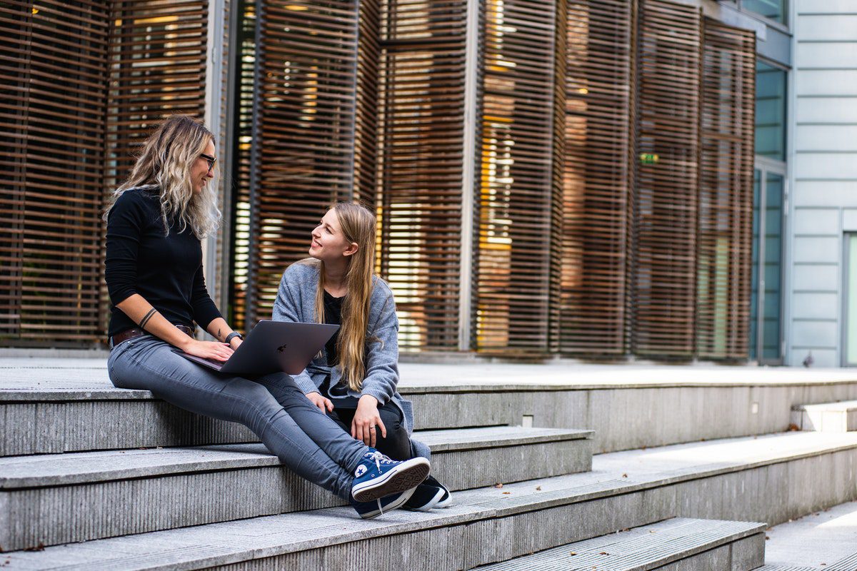 Two students sitting on the steps outside their university.