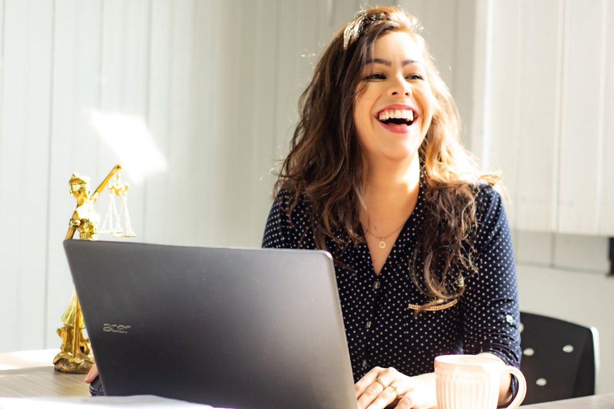 A woman working on a laptop and smiling in a sunny room