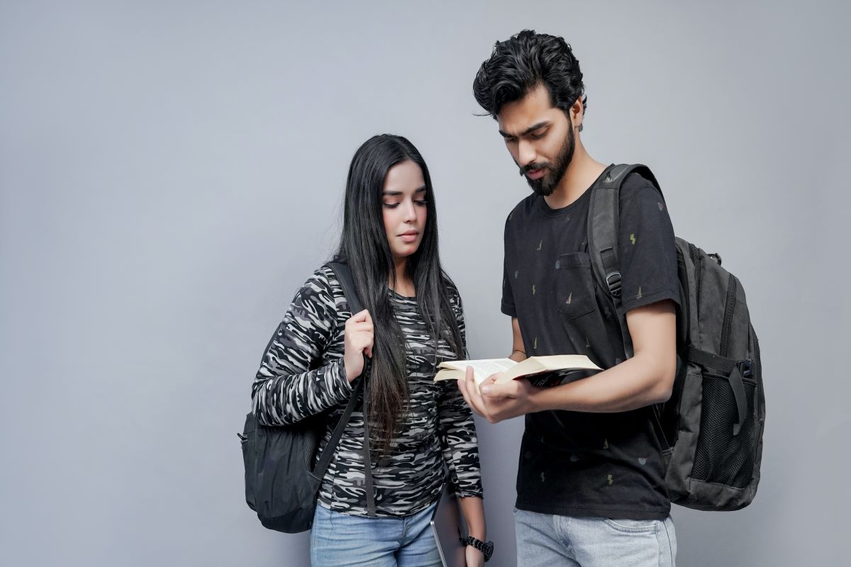 Two students in the residence hall looking at a textbook discussing their graduate program. 
