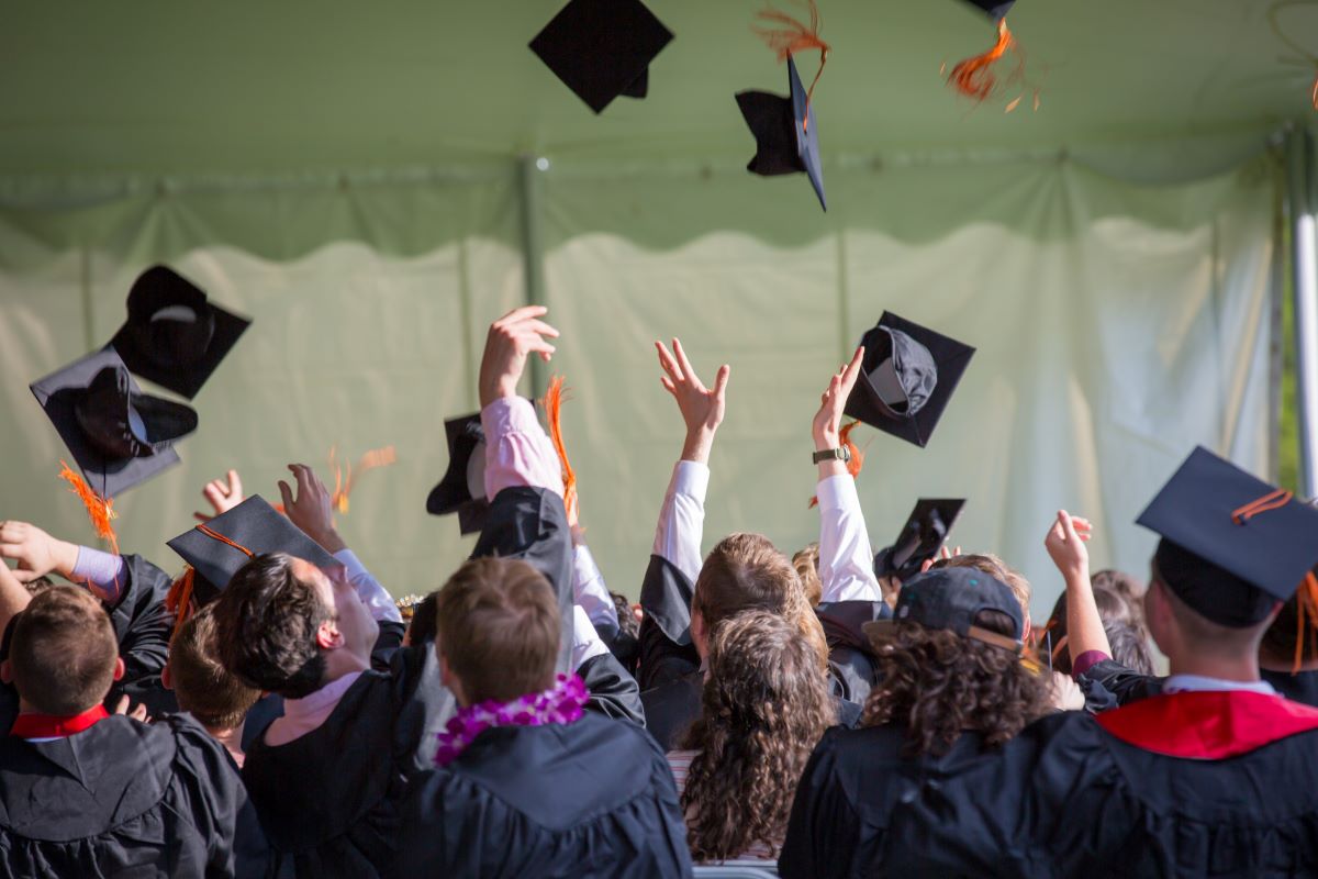 College students in black graduation gowns throwing their graduation caps into the air