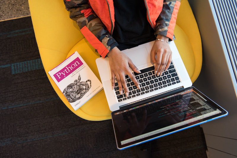 A person sitting at a cafe practicing coding next to a book on the Python programming language.