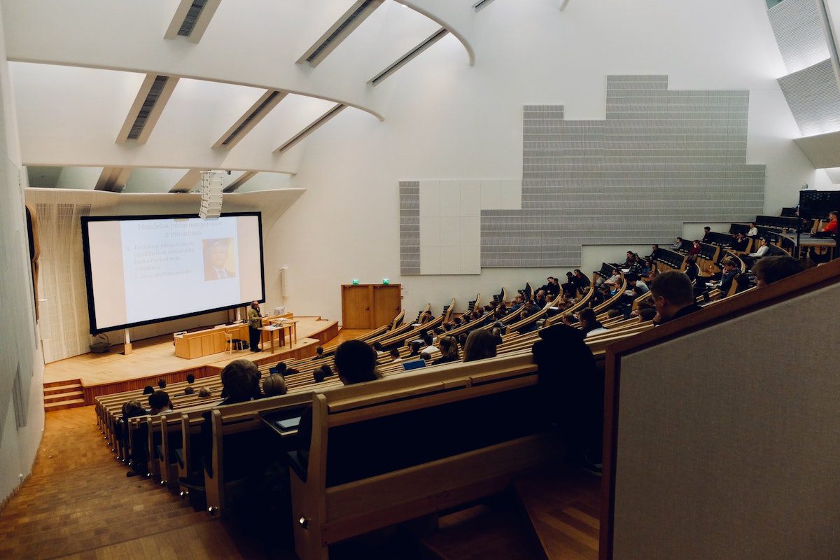 Students in a large classroom at a university, with a lecture projected on a screen in front of the class.
