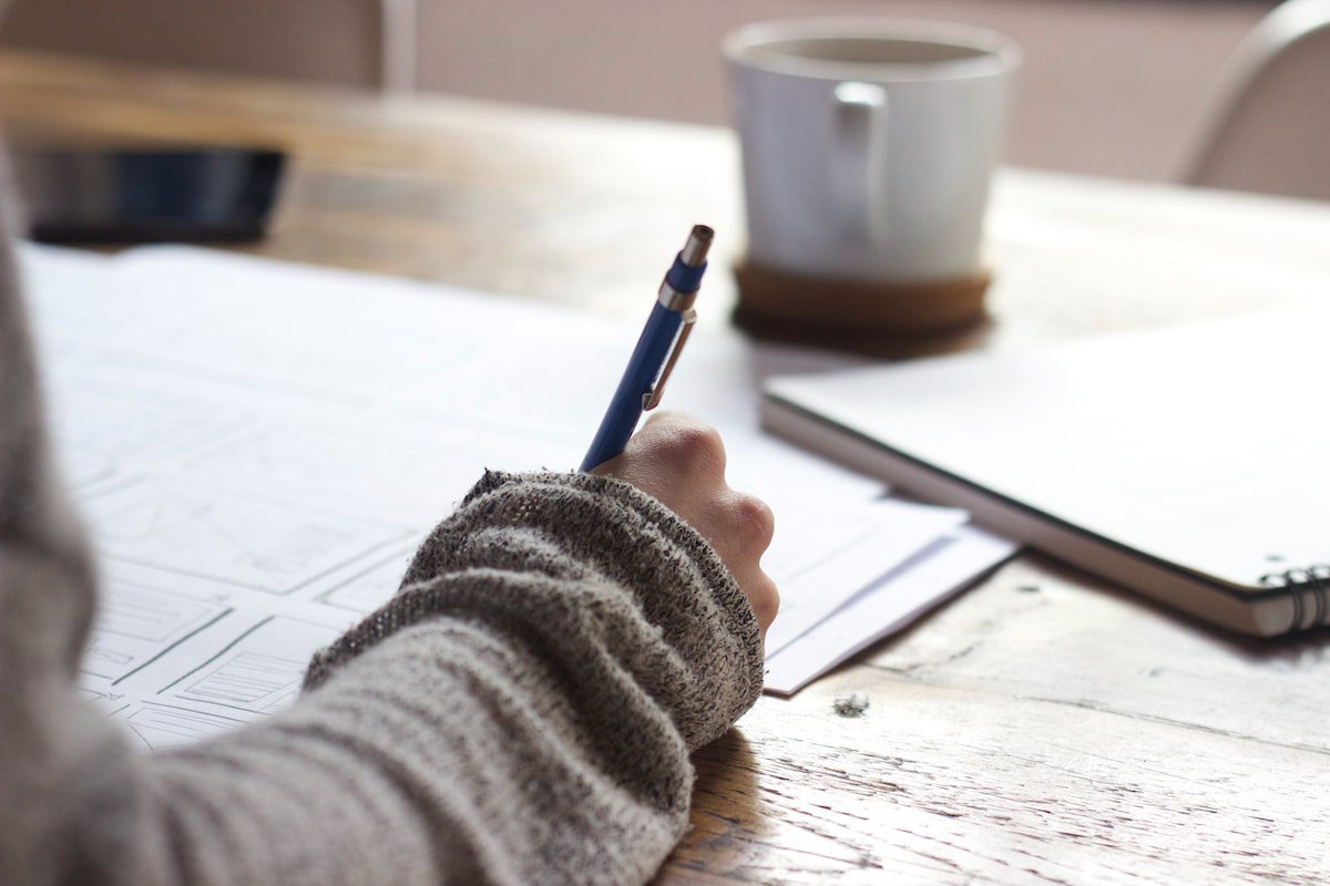 A person in a grey sweater writing with a pen.