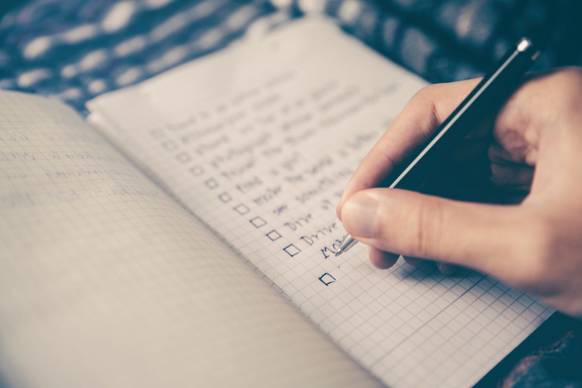 Close-up of person writing a university checklist in a notebook