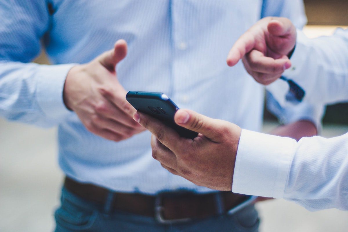 A person using a black phone to show another person a job description.