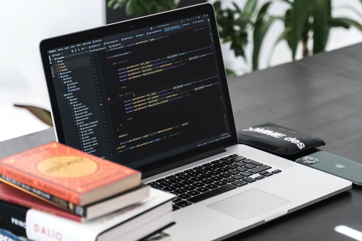 A laptop displaying multiple lines of codes next to a stack of coding books.