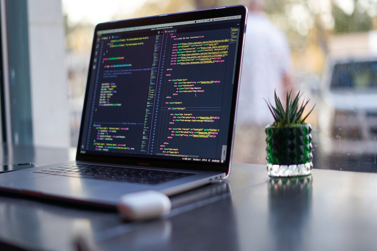 A laptop with GraphQL codes on a table with a plant 
