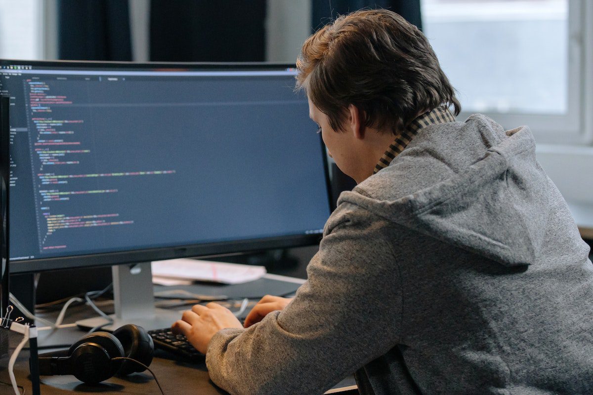 A man in gray hoodie coding on desktop and learning React basics.
