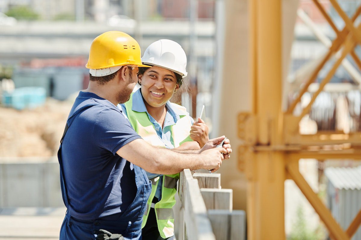 A woman smiling and talking to a man at a construction site.
