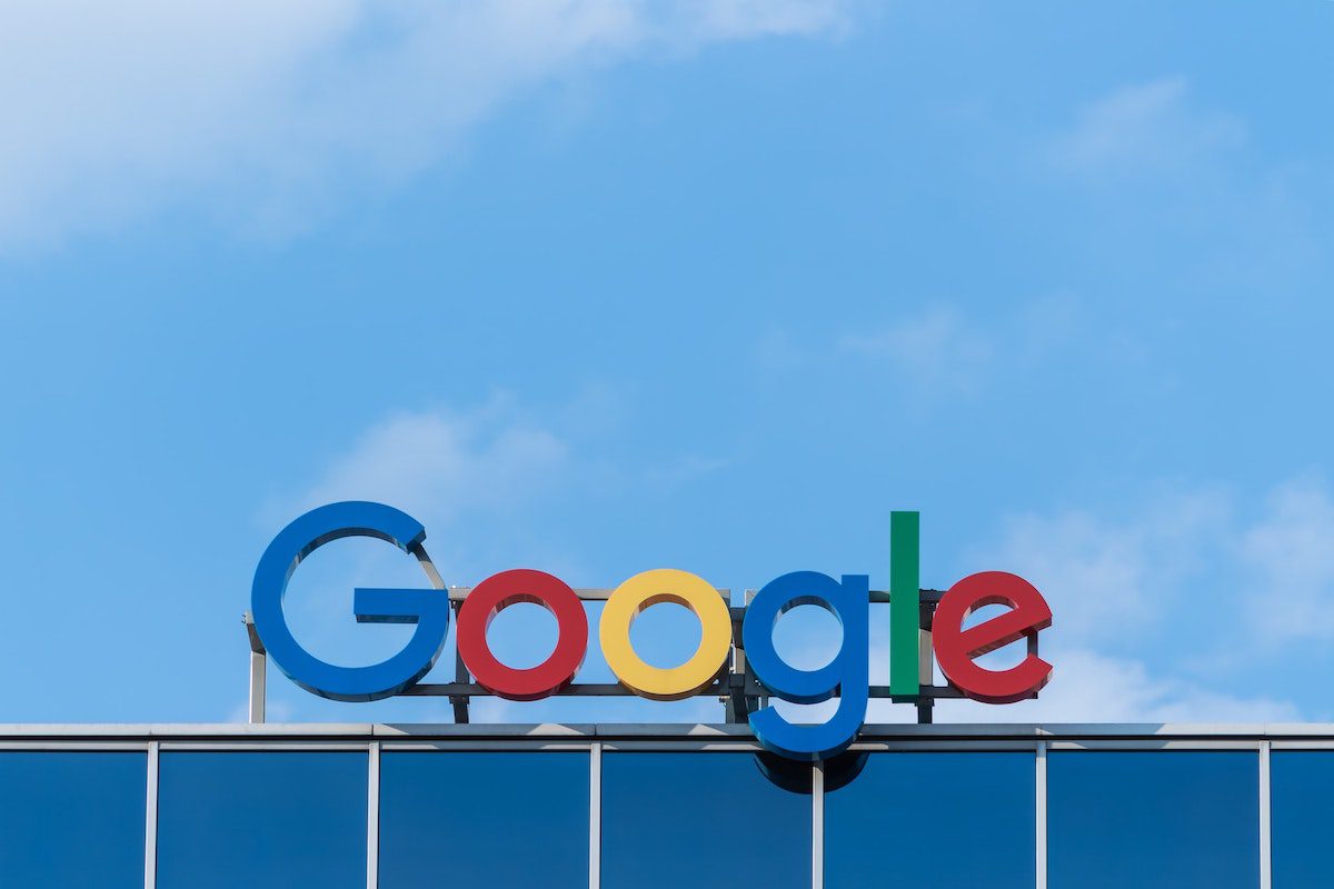 A sign of the Google logo on the top of a building with a blue sky in the background.
