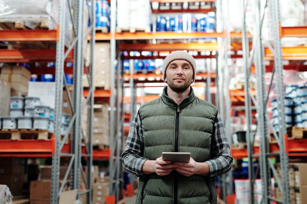 A Costco employee holding a tablet surrounded by warehouse goods. 