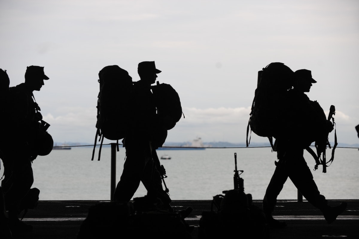 Silhouettes of soldiers carrying bulky backpacks.
