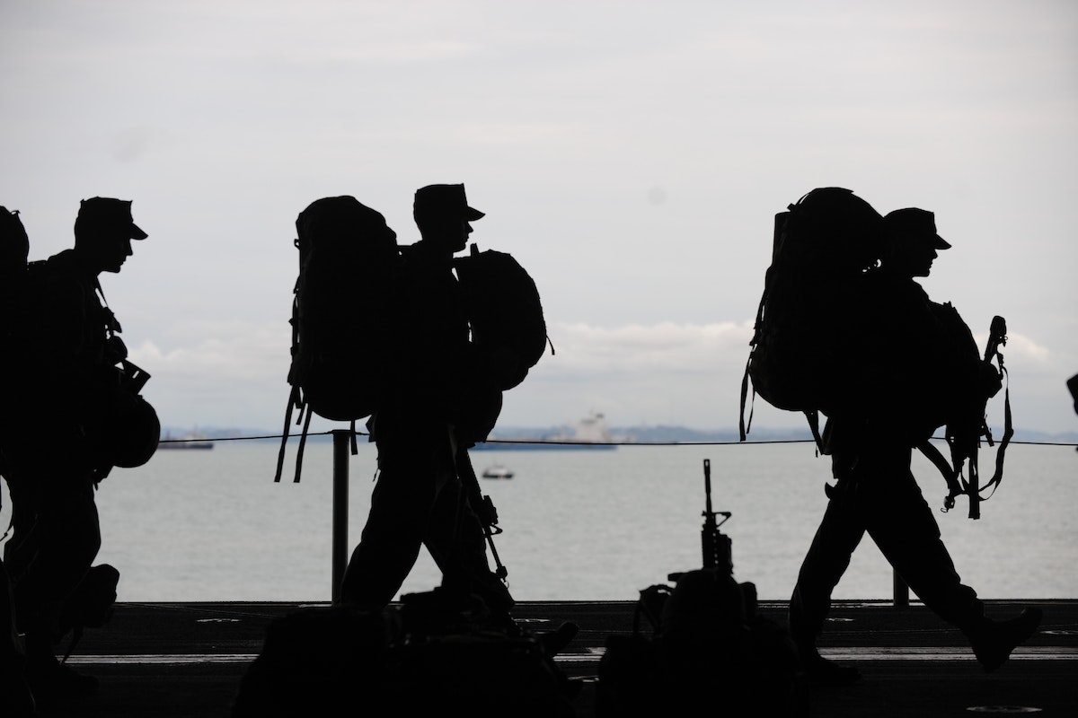 Silhouettes of soldiers carrying bulky backpacks. 